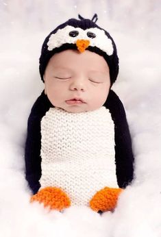 a baby is wearing a penguin hat and sleeping in the snow with it's eyes closed