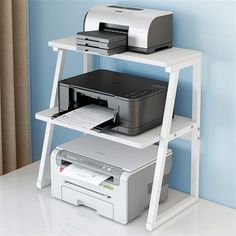 a computer desk with printer and scanners on top of it, in front of a blue wall