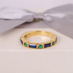 a gold ring with emeralds and blue sapphires on it, sitting next to a bow