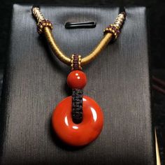 an orange and black necklace with gold accents on it's end, sitting on top of a metal box