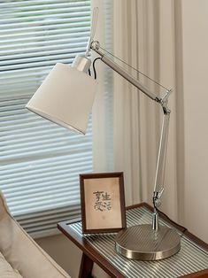 a desk lamp sitting on top of a wooden table next to a window with blinds