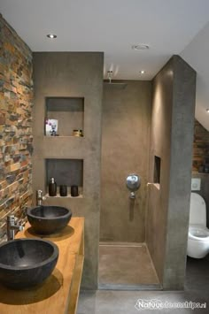 two black bowls are on the counter in this modern bathroom with stone walls and floor