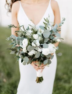 a woman in a white dress holding a bouquet of flowers and greenery on her wedding day