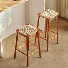 two wooden stools sitting next to each other on a carpeted floor in front of a window