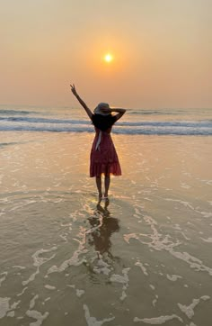 a woman standing in the ocean at sunset with her arms up and hands raised above her head