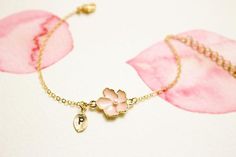 a gold bracelet with pink flowers on it and a pearl charm hanging from the clasp