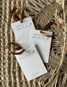 three white cards with brown ribbons and writing on them are sitting on a woven surface