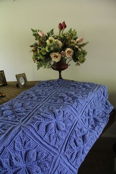 a blue crocheted blanket sitting on top of a table next to a vase with flowers