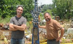 two men standing next to a large metal sculpture in the middle of a yard with trees