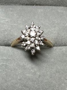 a diamond cluster ring sitting on top of a gray velvet cushion in a jewelry box