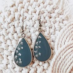 a pair of blue earrings with white flowers on them sitting on top of a blanket