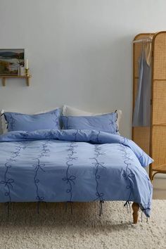 a bed with blue comforter and pillows in a room next to a wicker wardrobe