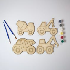 four wooden construction vehicles with paint and pencils on a white surface next to them