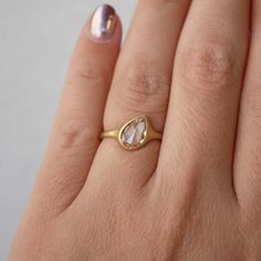 a woman's hand with a gold ring on it and a pink pearl in the middle