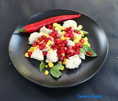 a black plate topped with cauliflower, corn and pomegranates