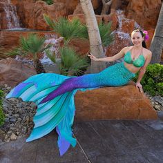 a woman dressed as a mermaid sitting on a rock with palm trees in the background