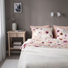 a bed with pink and white flowers on it in a bedroom next to a window