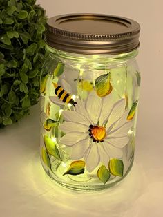 a glass jar with flowers painted on it next to a potted plant and green leaves