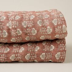 two pink bedspreads with white flowers on them, one is folded up and the other has a pillow