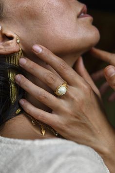 a close up of a person wearing gold jewelry and holding her hand to her ear