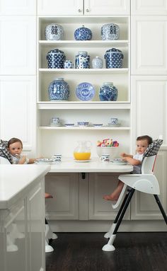 two children sitting at a kitchen table with blue and white dishes on the shelves behind them