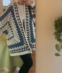 a woman standing next to a wall holding a cell phone up to her ear and wearing a crocheted sweater