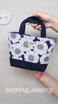 a hand holding a blue and white flowered bag with the word spring on it