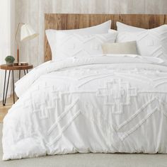 a bed with white comforter and pillows in a room next to a lamp on a table