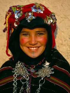 a woman wearing a red and black headdress with flowers on her hair smiling