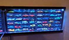 there are many toy cars on display in the glass case that's lit up