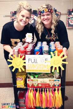 two girls are standing behind a cooler with sun decorations on it and some drinks in front of them