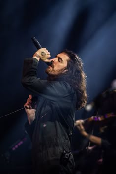 a man with long hair holding a microphone in his right hand while standing on stage