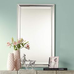 a vase with flowers on top of a dresser next to a mirror and photo frame