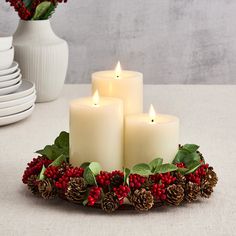 three lit candles sitting on top of a tray with pine cones and holly wreaths