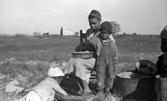 an old black and white photo of three children in a field with buckets full of food