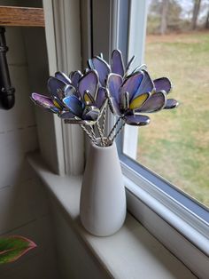 a white vase filled with purple flowers on top of a window sill