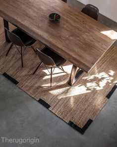 a wooden table with chairs and a rug on the floor in front of it that has a potted plant next to it