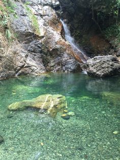 the water is crystal green and there are many rocks in front of it, with a waterfall