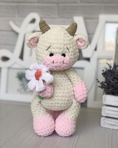 a crocheted stuffed cow with a flower in it's hand sitting on a table