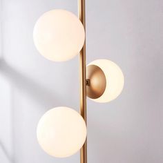 three white balls are hanging from a brass pole with one light on top and the other off to the side