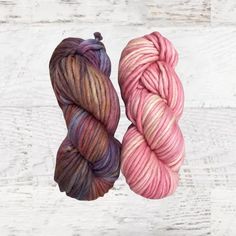 two skeins of yarn sitting next to each other on a white wooden surface