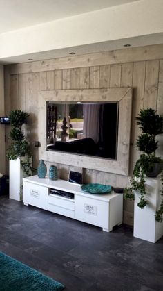 a flat screen tv mounted to the side of a wall next to potted plants