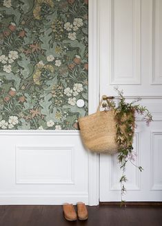 a basket hanging on the wall next to a flowered wallpaper with white paneling