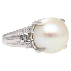 15mm South Sea Pearl and Diamond Platinum 900 Cocktail Ring. Featuring a lustrous 15mm south sea white pearl center stone, secured in a prong setting. The pearl is paired with 4 round cut and 4 baguette cut natural diamonds. The pearl is secured in a basket setting with a heart shape motif, and half bezel set diamonds and share weight of 0.46 carats. The ring is crafted from platinum 900. The pearl has phenomenal uniformity and symmetry. Set in a platinum 900 that offers supreme durability and s White Pearl Ring With Diamond Accents And Akoya Pearl, Classic White Pearl Ring With Diamond Accents, Luxury White Rings With Pearl Drop, Timeless White Round Cut Pearl Ring, White Timeless Round Cut Pearl Ring, Timeless Pearl Ring With Diamond Accents For Formal Occasions, Formal White Pearl Ring, Luxury Round Ring With Pearl Drop, Luxury Round Pearl Drop Ring