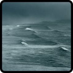 black and white photograph of ocean waves in the distance with dark clouds above it,