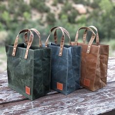 three bags sitting on top of a wooden table next to each other and one has a brown leather handle