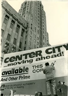 a man is painting the side of a large sign in front of a tall building