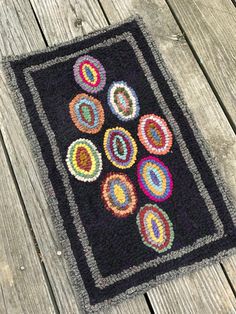 a black rug with multicolored circles on it sitting on a wooden floor next to a fence