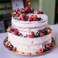 a three tiered cake with strawberries and blueberries on top sits on a table