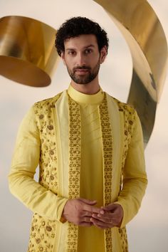 Summer Love Shrug Set | Jatin Malik Introducing our vibrant lemon yellow shrug set, adorned with intricate floral hand embroidery and three types of embroidered lapels in shades of yellow. This ensemble radiates freshness and sophistication, capturing attention with its intricate detailing and vibrant color palette. Paired with an embroidered shoulder-button kurta and tapered trousers, this outfit offers a perfect balance of elegance and contemporary style. Ideal for special occasions, this ensemble is sure to make a statement with its unique design and impeccable craftsmanship. Included in purchase: Shrug Set, Kurta, Trousers Product Specification Color: Yellow Fabric: Linen Silk Occasion: Engagement, Wedding, Bridal, Reception Style: Shrug Set, Kurta, Trousers Care: Dry Clean Work: Hand Yellow Cutdana Sets For Reception, Yellow Traditional Wear With Cutdana And Long Sleeves, Designer Yellow Sherwani For Eid, Transitional Designer Wear Yellow Sherwani, Yellow Designer Sherwani With Traditional Drape, Yellow Sherwani With Traditional Drape, Yellow Kurta For Diwali Reception, Designer Sets With Floral Embroidery And Traditional Drape, Elegant Yellow Designer Wear Sets